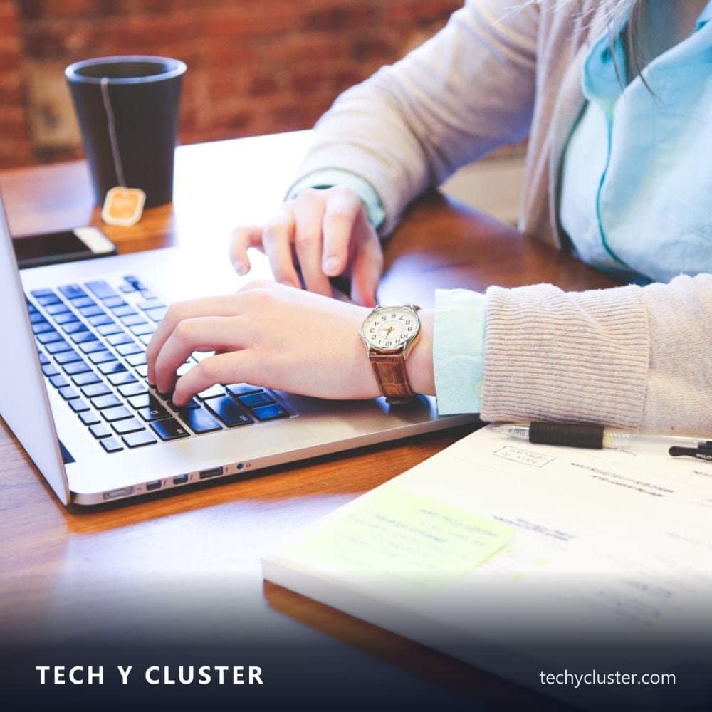 Person typing on a laptop beside a notebook