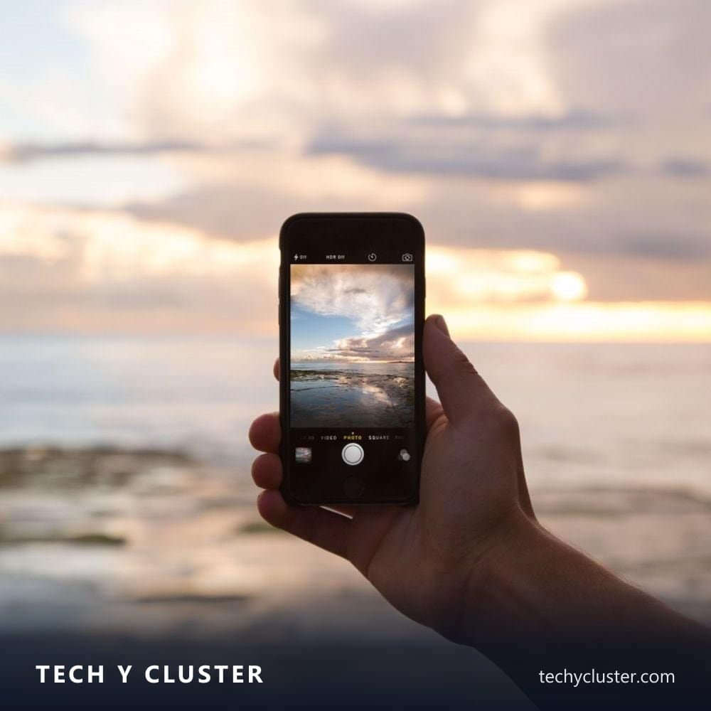 Hand holding a smartphone taking a photo of a sunset over the sea