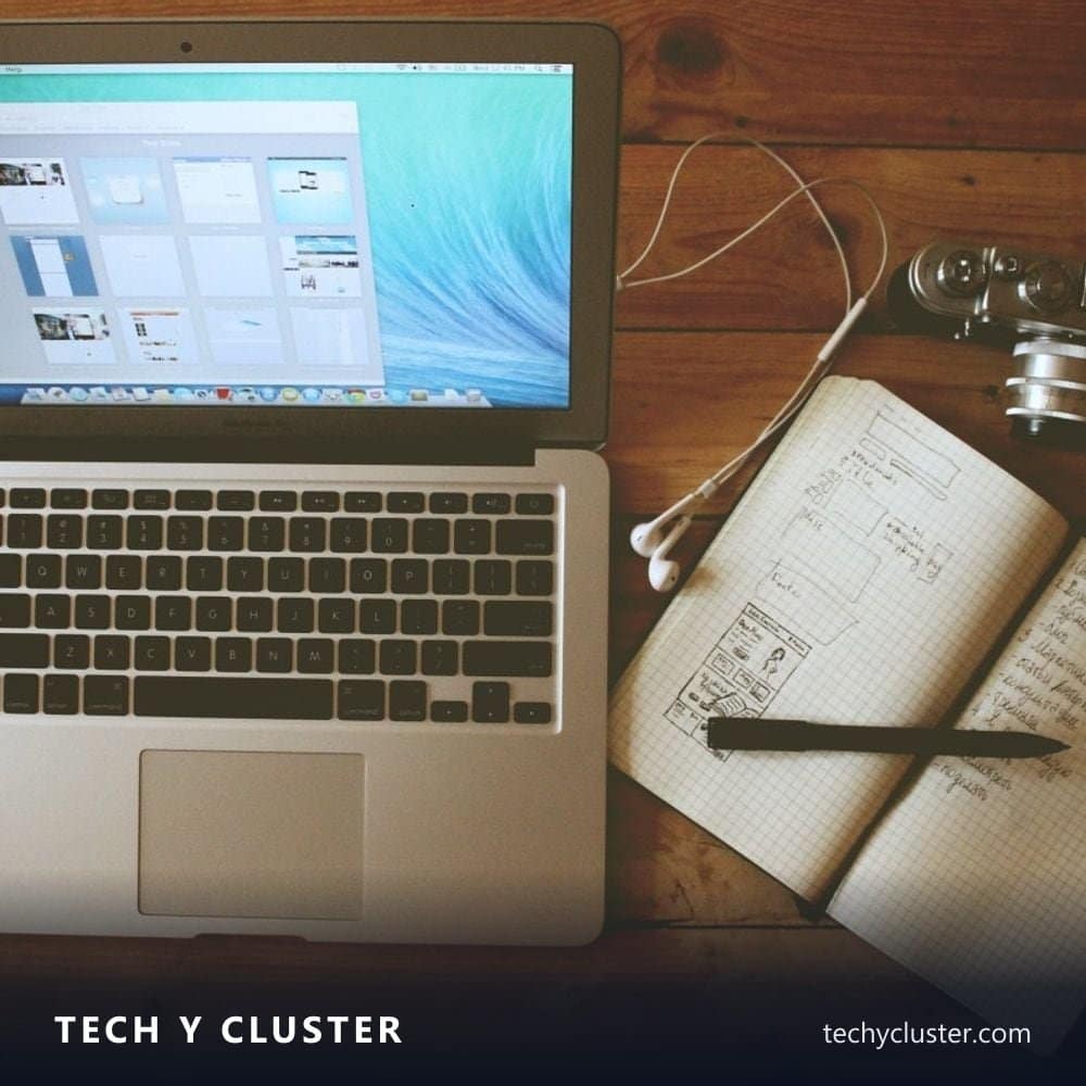 Laptop on a wooden desk beside a notebook and earphones